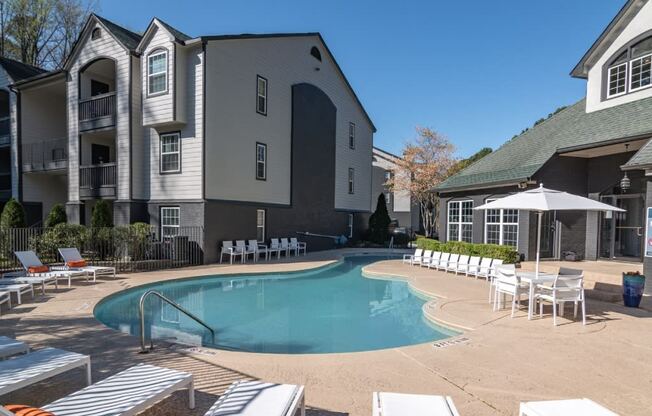 a large swimming pool with chairs and umbrellas in front of a building