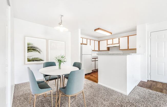 Model Apartment with Dinette Table in Front of Framed Wall Art Next to Open Kitchen with White Cabinets with Wood Accents and White Appliances