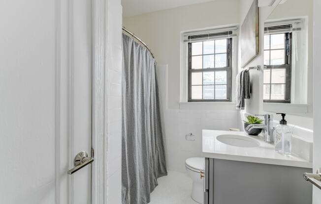 bathroom with toilet, vanity, tub, and window at the dahlia apartments in washington dc