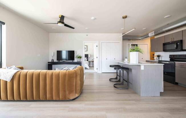A modern living room with a brown sofa and a kitchen in the background.