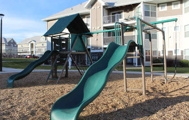 a playground with slides and swings in front of a building