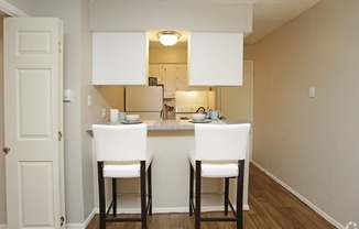 a kitchen with white cabinets and a counter with two chairs