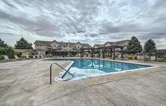 Pet-Friendly Apartments in Aurora, CO– Aurora Meadows – A large outdoor swimming pool surrounded by a concrete patio and a resort-style building in the background.
