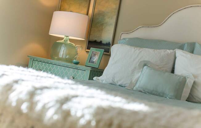 A bed with white pillows and a green lamp on a nightstand.