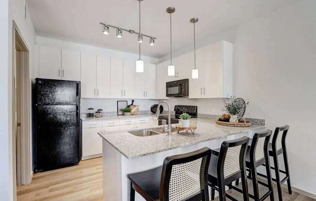 A kitchen with a black fridge, white cabinets, and a marble countertop.