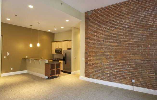 an empty living room with a brick wall and a kitchen at The Granite Works Apartments , New York 14202