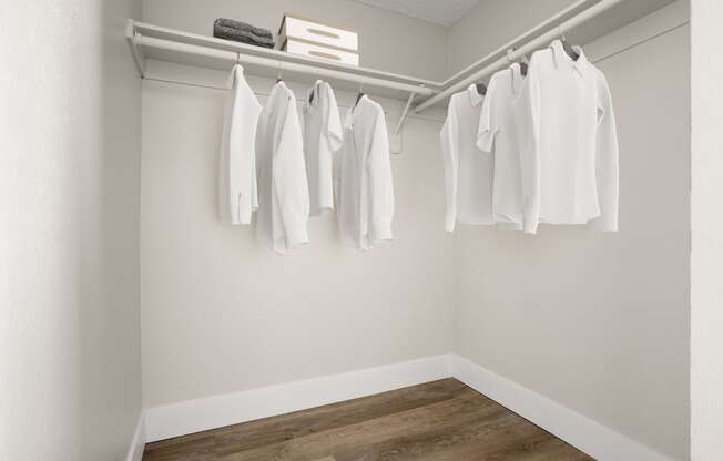 a walk in closet with white clothes hanging on a rail