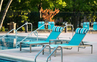 a pool with blue chaise lounge chairs and a poolside table