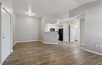 A spacious room with wooden flooring and a kitchenette in the background.