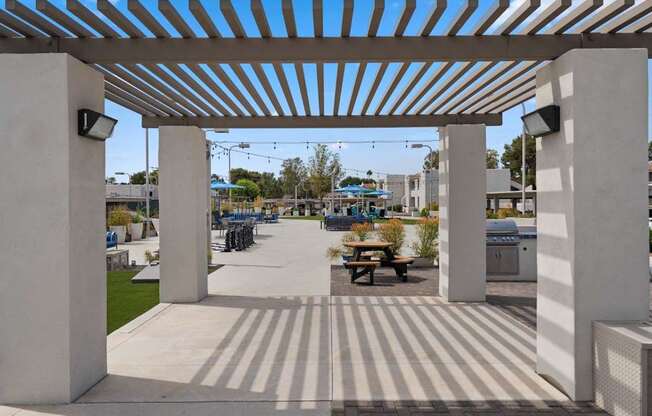 A white pergola with a striped floor and a picnic table underneath.