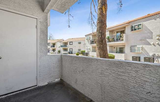A white door is on the left of a balcony with a tree in the background.