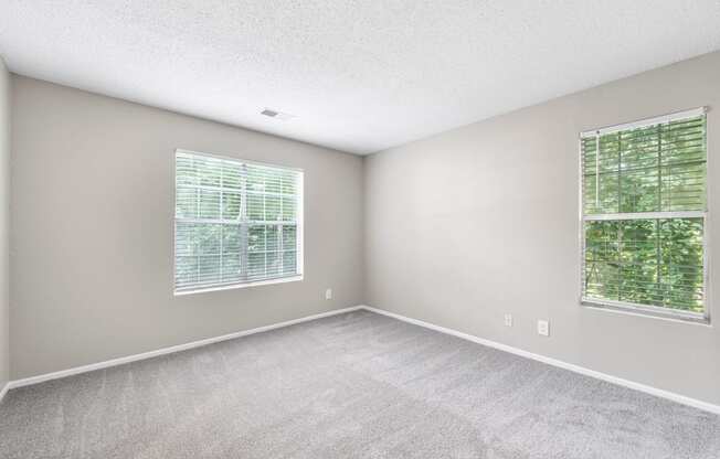 an empty bedroom with two windows and carpeting