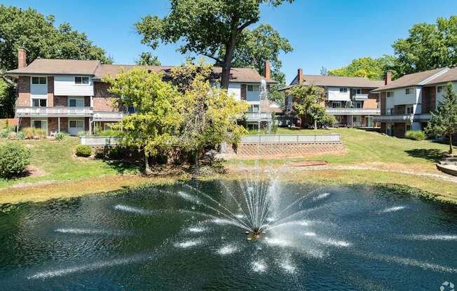 A fountain in the middle of a pond in front of apartment buildings.
