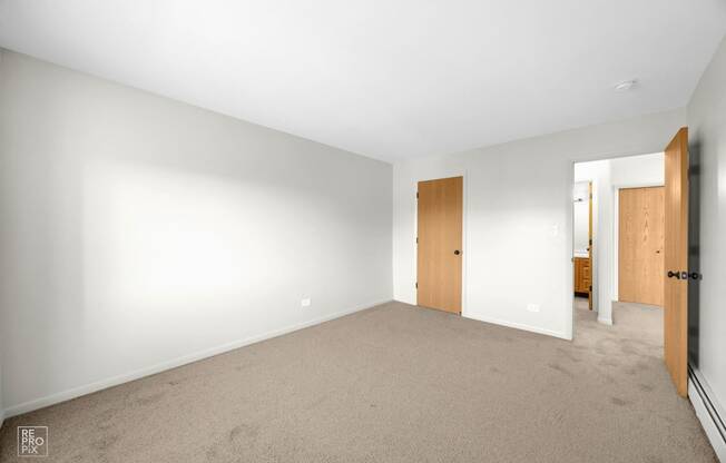 a bedroom with white walls and carpet and a door to a bathroom