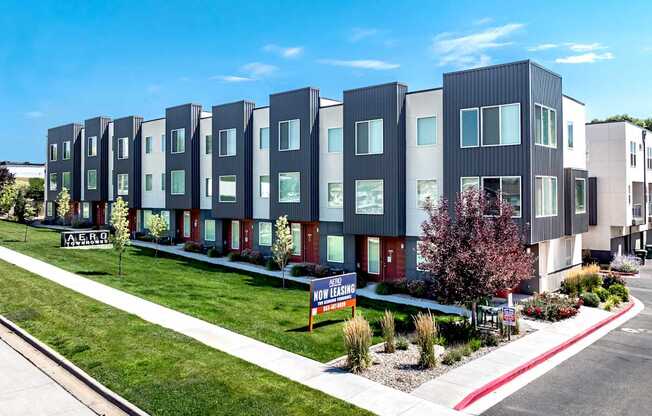 A row of modern townhouses with a "For Sale" sign in front.