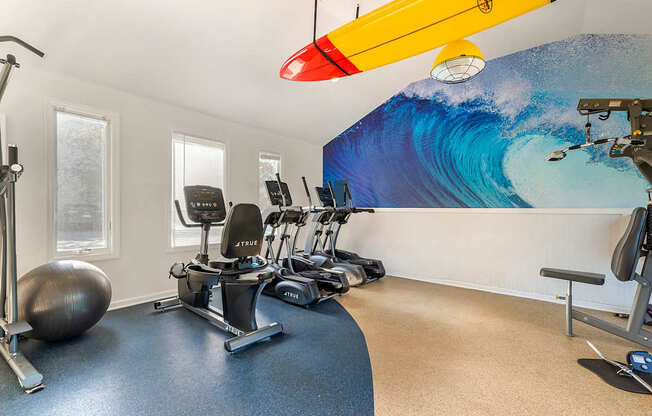 a gym with exercise machines and a surfboard on the wall