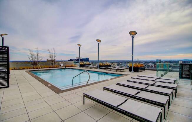 A pool with sun loungers and lights on the side.