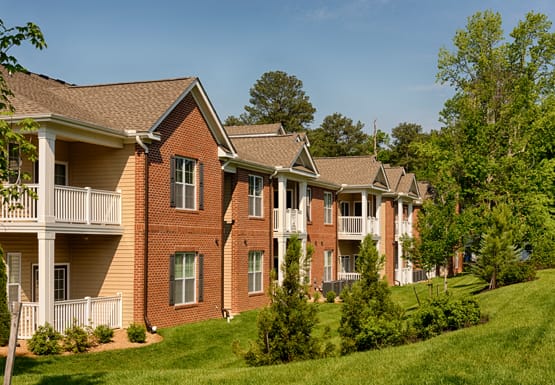 Apartment exterior with balconies and patios; overlooking a grassy area with trees