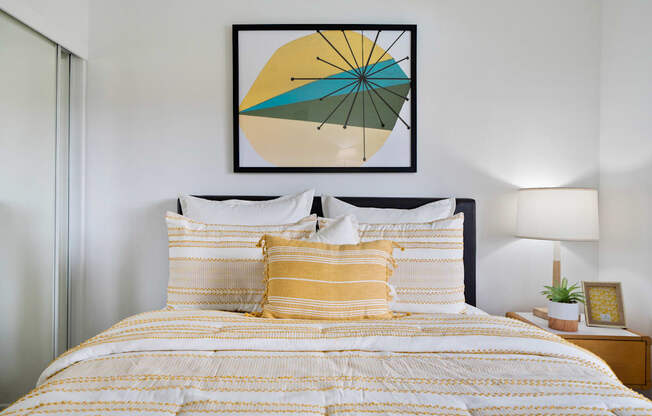 a bedroom with a bed with yellow and white bedding and a framed picture above the bed