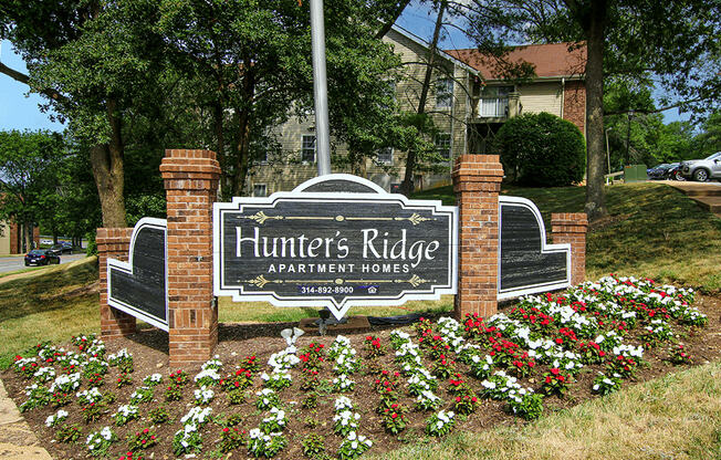 a sign for hunters ridge apartment house in front of a flower garden