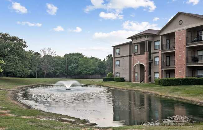 a pond with a fountain in front of an apartment building