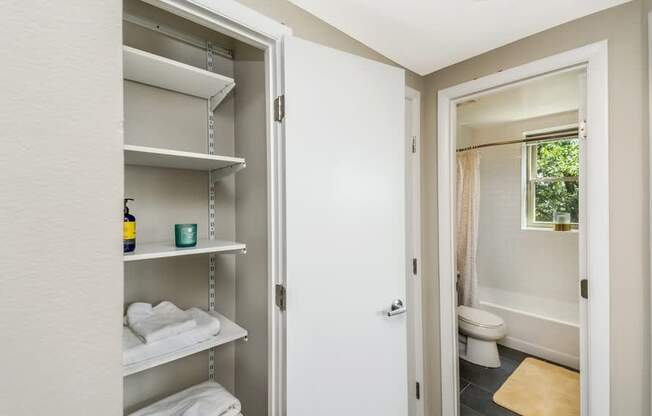 A white bathroom with a white door and a white shelving unit with towels and a bottle.