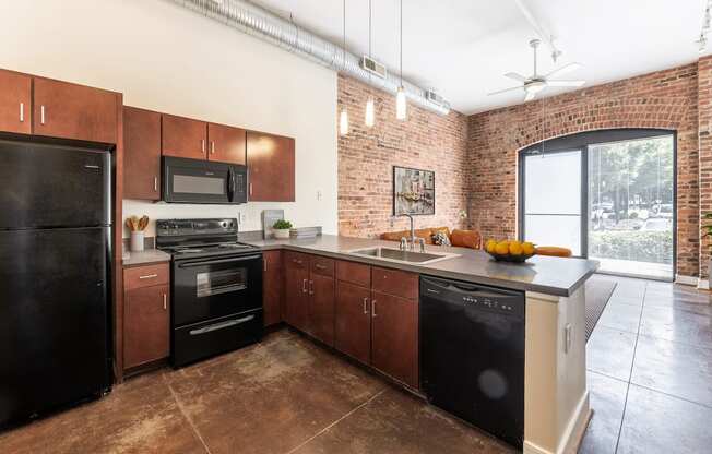 a kitchen with black appliances and wooden cabinets and a brick wall