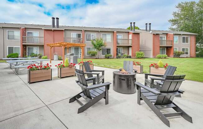 A patio with chairs and a fire pit in front of apartment buildings.