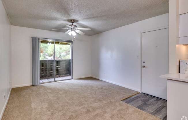 an empty living room with a door to a balcony and a ceiling fan