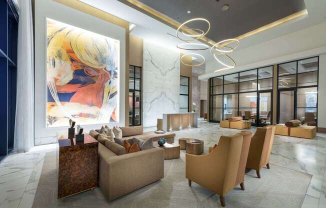 Spacious lobby with high ceilings, floor-to-ceiling windows, marble floors and wall cladding, colorful modern art, a concierge desk, and multiple sitting areas with couches, armchairs, and coffee tables.