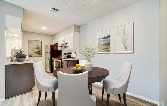 a dining area with a table and chairs and a kitchen in the background