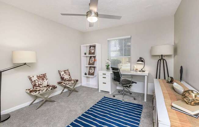 A room with a desk, chairs, and a ceiling fan.