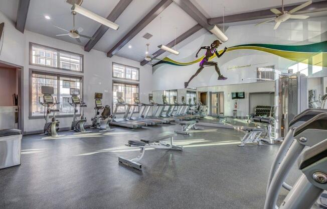 Large fitness center with concrete flooring and ceiling fans. Weight benches, yoga balls, and cardio machines