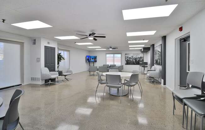 A room with a white ceiling and a grey floor with chairs and tables.