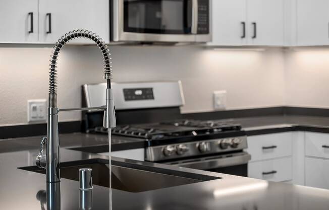 a kitchen with a sink with a gooseneck style faucet with water turned on and a stove in the distance