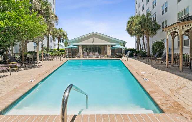 A large swimming pool surrounded by a brick patio and lounge chairs.