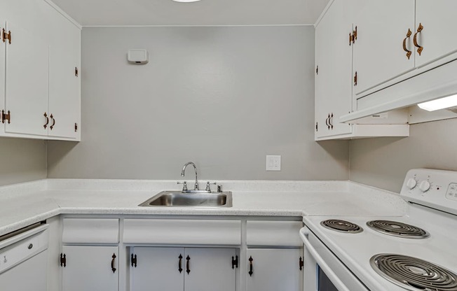 A kitchen with white cabinets and a white stove top oven.