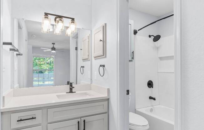 A white bathroom with a sink, mirror, and toilet.