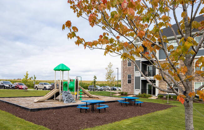 a playground with a slide and picnic table in front of a building