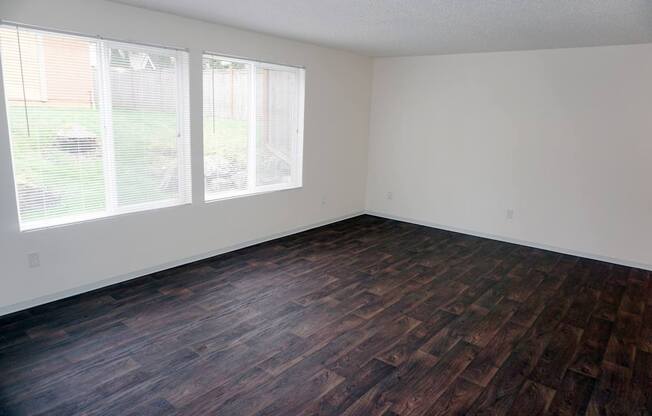 an empty room with wood flooring and two windows