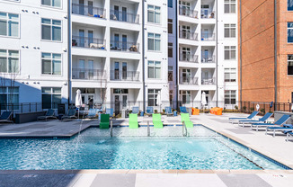 a swimming pool with green chairs in front of an apartment building