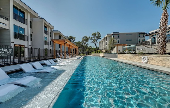 a large pool with lounge chairs in front of apartment buildings