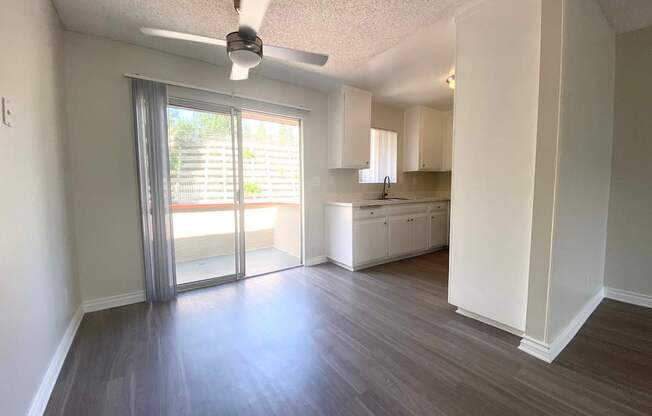 an empty living room with a sliding glass door to a kitchen