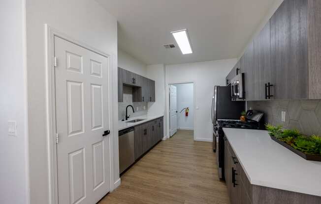 an open door leading into a kitchen with dark cabinets and a white counter top