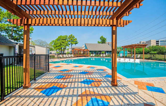 A pool area with a colorful tile walkway and a wooden pergola.