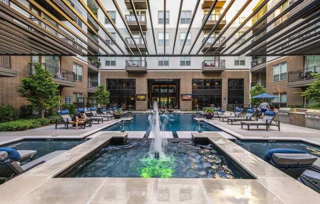 a pool with a fountain and lounge chairs in front of an apartment building