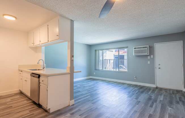 an empty living room with a kitchen and a window