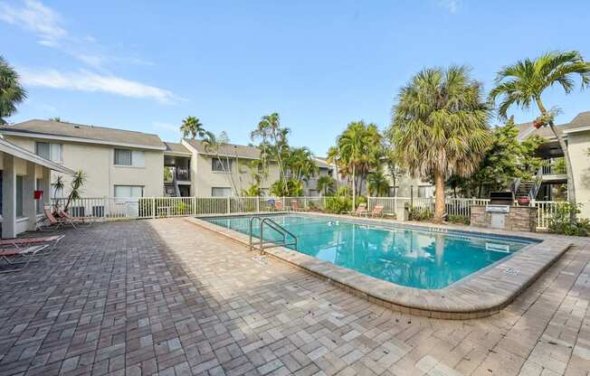 A swimming pool surrounded by a brick patio and palm trees.