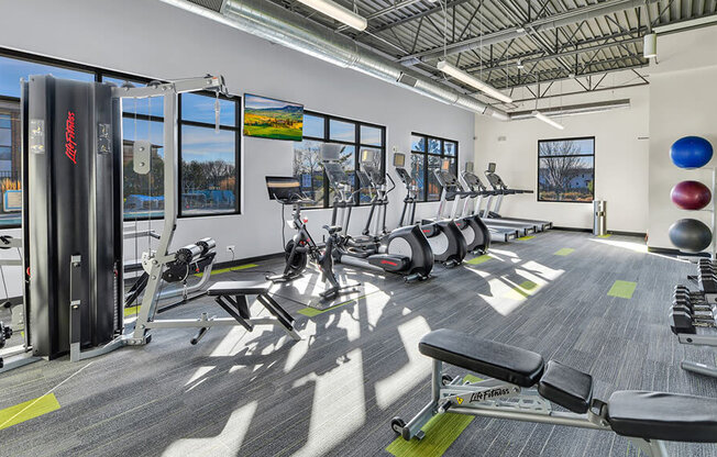 a workout room with cardio equipment and windows