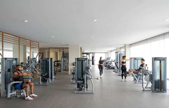 A man is working out in a gym with a woman stretching in the background. at Palma, Doral, FL, 33166